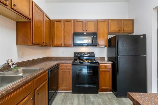 kitchen with a sink, light wood-type flooring, black appliances, brown cabinetry, and dark countertops