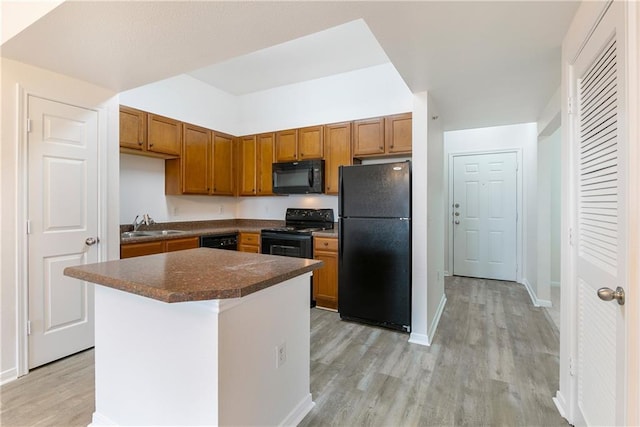 kitchen with dark countertops, a sink, a kitchen island, light wood-type flooring, and black appliances