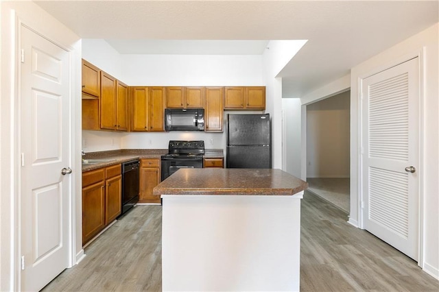 kitchen with brown cabinets, dark countertops, light wood-style floors, a kitchen island, and black appliances