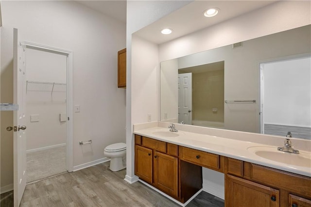 bathroom featuring toilet, double vanity, a sink, and wood finished floors