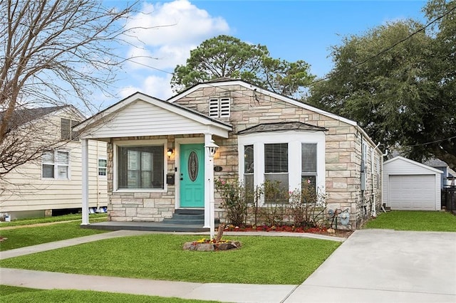 bungalow-style home with driveway, stone siding, a front yard, and an outbuilding