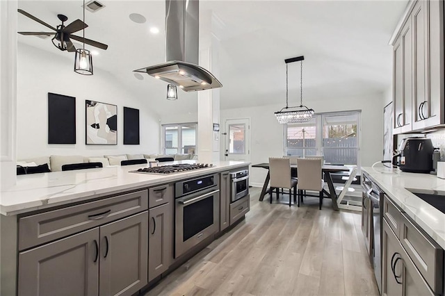 kitchen featuring hanging light fixtures, light stone countertops, island exhaust hood, gray cabinets, and stainless steel appliances