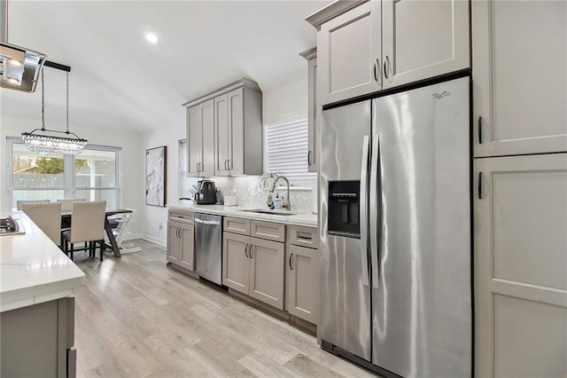 kitchen with stainless steel appliances, a sink, light countertops, gray cabinets, and decorative backsplash