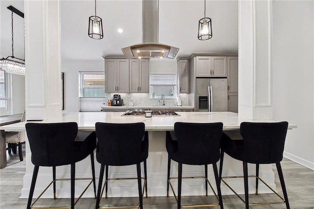 kitchen with island range hood, gray cabinetry, a breakfast bar, hanging light fixtures, and appliances with stainless steel finishes