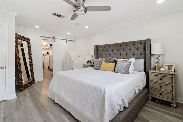 bedroom featuring wood finished floors, visible vents, crown molding, and a barn door