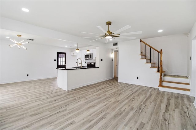 unfurnished living room with stairway, a sink, light wood-style flooring, and baseboards