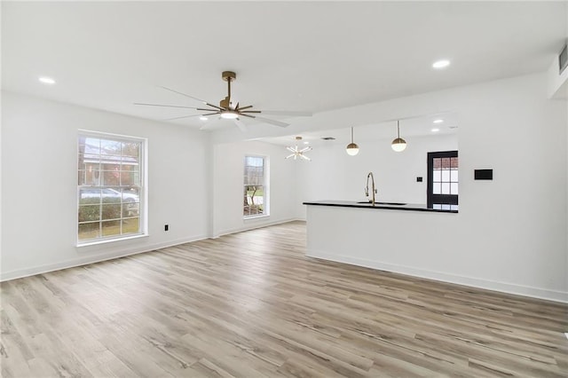 unfurnished living room featuring recessed lighting, a sink, light wood-type flooring, baseboards, and ceiling fan with notable chandelier