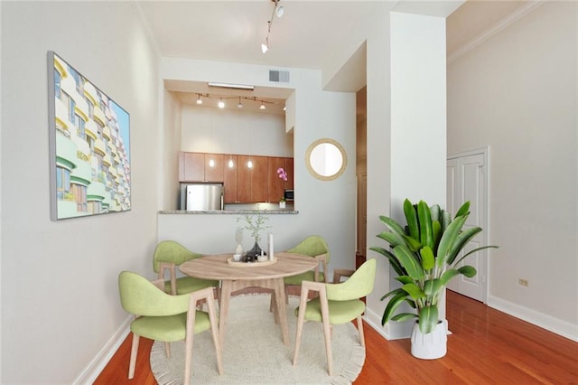 dining room featuring visible vents, track lighting, baseboards, a high ceiling, and wood finished floors