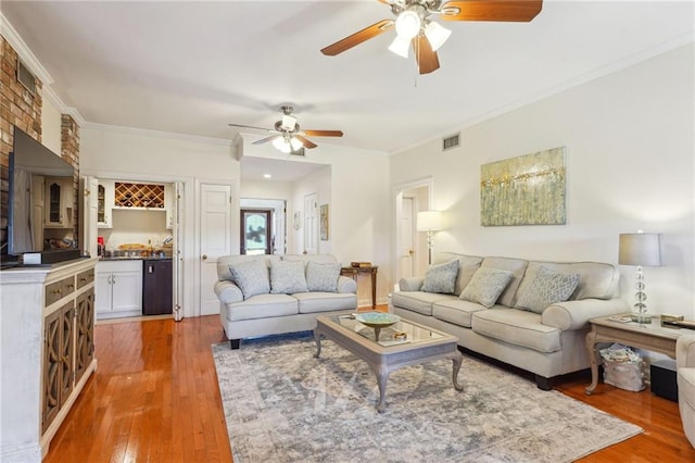 living area featuring visible vents, indoor bar, wood finished floors, and ornamental molding