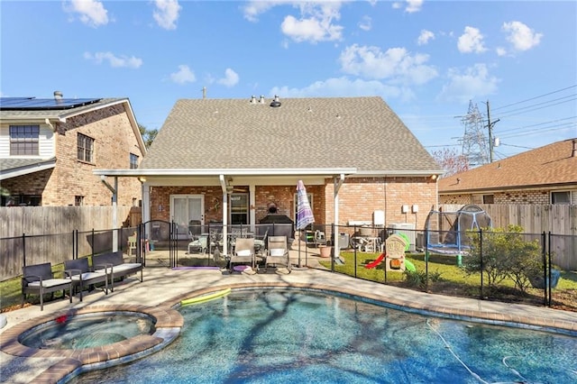 rear view of house with a patio, a fenced backyard, brick siding, a pool with connected hot tub, and roof with shingles