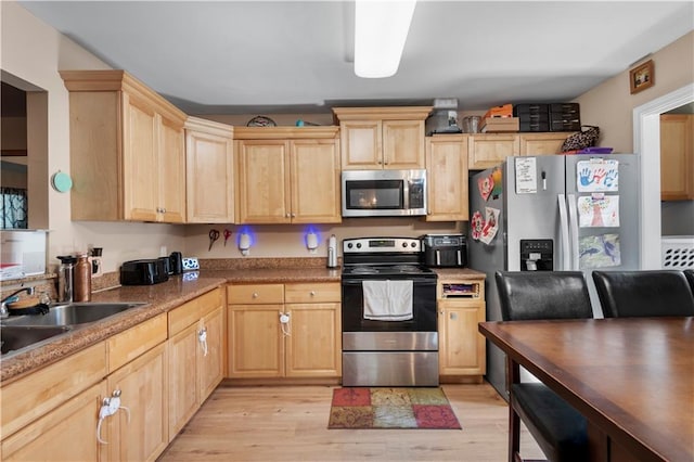 kitchen with appliances with stainless steel finishes, light countertops, light wood-type flooring, light brown cabinets, and a sink