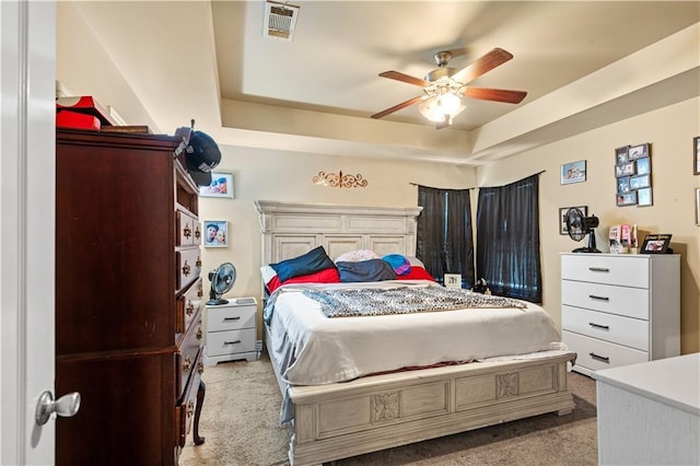 bedroom featuring visible vents, a raised ceiling, a ceiling fan, and light colored carpet