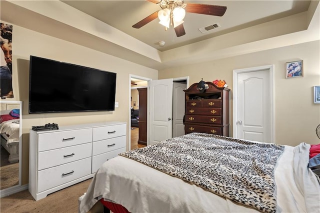 bedroom featuring a tray ceiling, visible vents, ceiling fan, and carpet