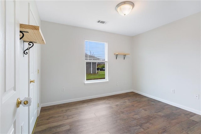 empty room with dark wood-style floors, visible vents, and baseboards