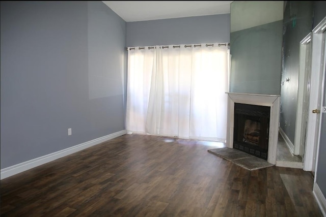 unfurnished living room with dark wood-type flooring, a fireplace with raised hearth, and baseboards