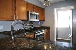 kitchen featuring stainless steel appliances, brown cabinetry, and dark stone countertops