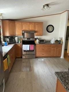 kitchen with stainless steel electric range oven, dark countertops, light wood-style flooring, brown cabinetry, and under cabinet range hood