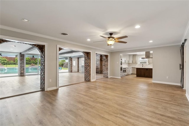 unfurnished living room featuring light wood-style flooring, a sink, visible vents, baseboards, and ornamental molding