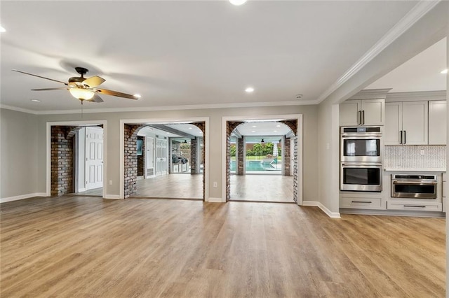 unfurnished living room with crown molding, baseboards, a ceiling fan, and light wood-style floors