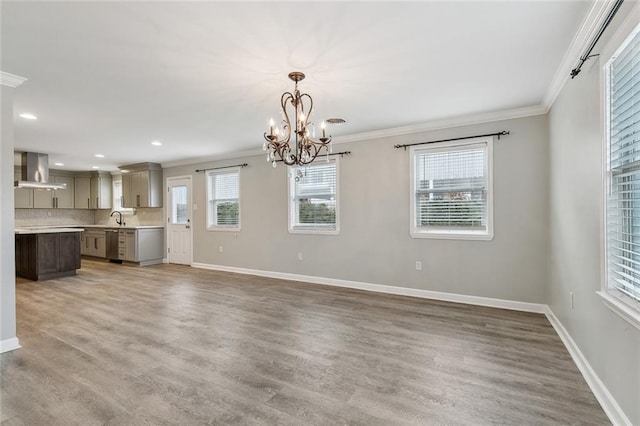 unfurnished living room with baseboards, ornamental molding, wood finished floors, an inviting chandelier, and recessed lighting