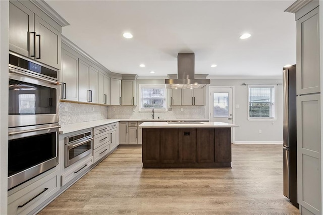 kitchen featuring stainless steel appliances, island range hood, light countertops, and gray cabinetry