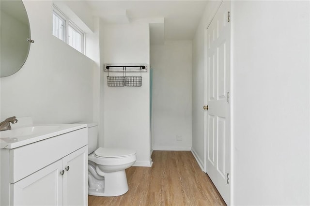 half bathroom with baseboards, vanity, toilet, and wood finished floors