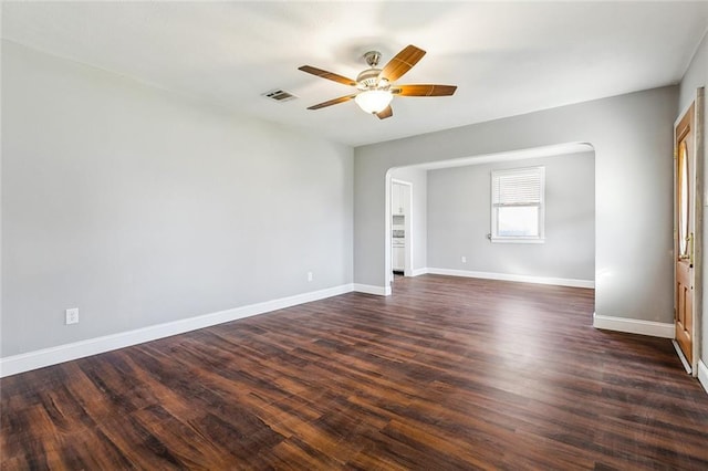 spare room with a ceiling fan, visible vents, baseboards, and dark wood-type flooring