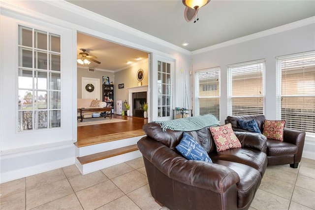 living area with a fireplace, light tile patterned floors, ornamental molding, a ceiling fan, and baseboards