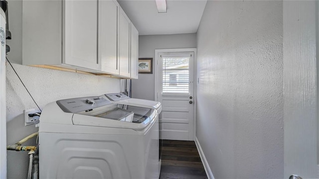 clothes washing area featuring a textured wall, washing machine and dryer, baseboards, cabinet space, and dark wood-style floors