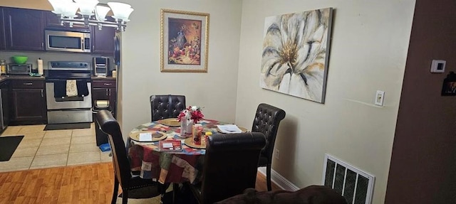 dining room with light wood-type flooring, an inviting chandelier, a toaster, and visible vents