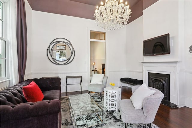living room featuring a chandelier, wood finished floors, a fireplace with raised hearth, and a wainscoted wall