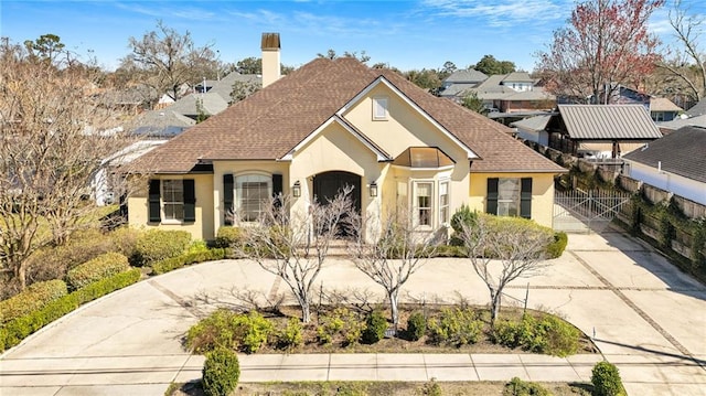 view of front of property featuring driveway, a shingled roof, a chimney, a gate, and stucco siding