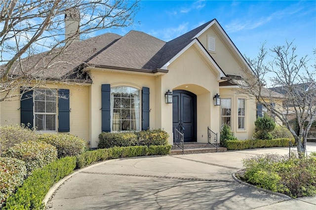 view of front of home featuring a shingled roof, driveway, a chimney, and stucco siding