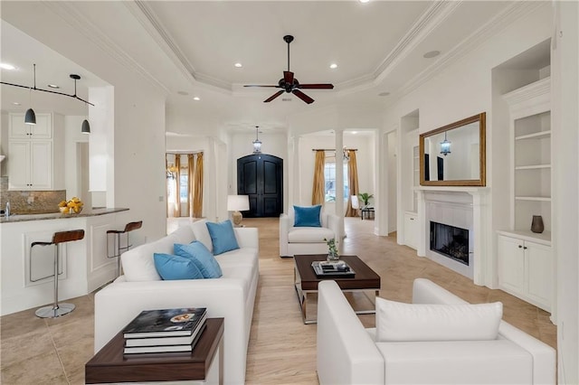 living area featuring crown molding, a fireplace, built in features, and a tray ceiling