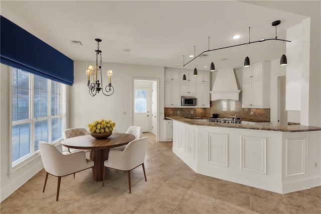 kitchen with white cabinets, custom exhaust hood, decorative backsplash, stainless steel microwave, and dark stone countertops