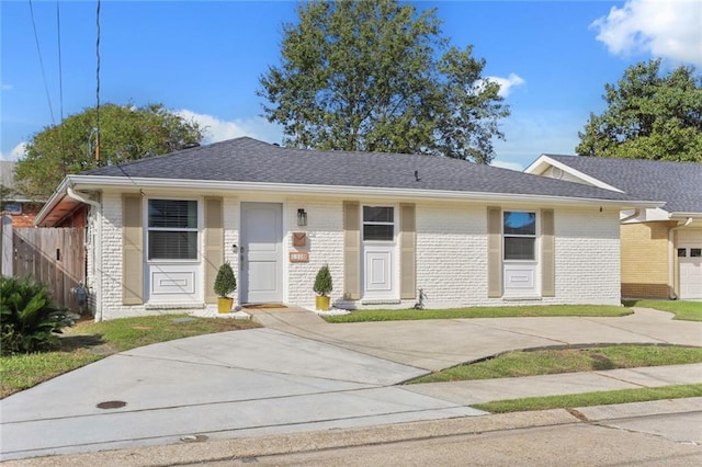 ranch-style home featuring driveway, brick siding, roof with shingles, and fence