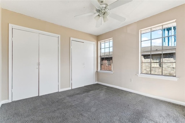 unfurnished bedroom with carpet, baseboards, ceiling fan, and two closets