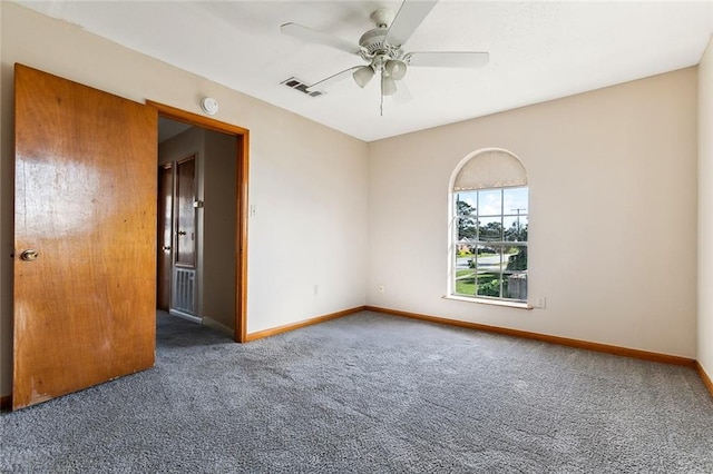 spare room with a ceiling fan, visible vents, dark carpet, and baseboards