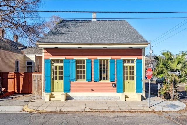 view of front of property with entry steps, a shingled roof, and fence