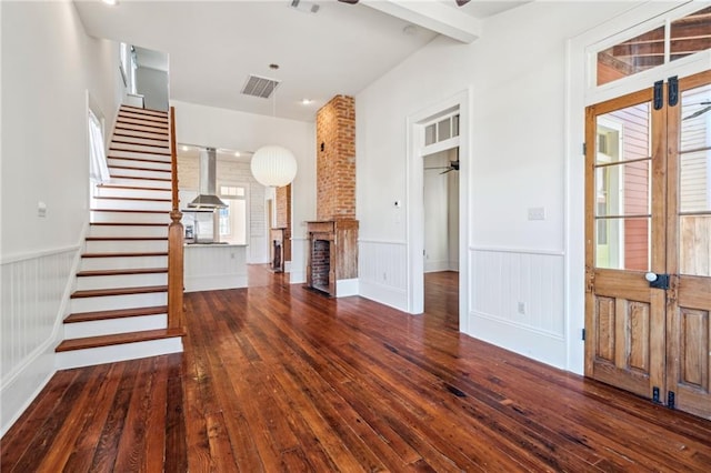 3829 Dauphine St, New Orleans, LA 70117 - unfurnished living room featuring french doors, dark wood-type flooring, a brick fireplace, wainscoting, and stairs