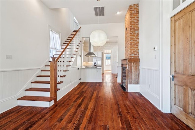 foyer entrance with a wainscoted wall, stairway, dark wood-style floors, and visible vents