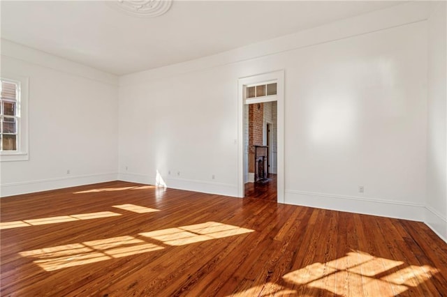 empty room with a fireplace, baseboards, and wood finished floors