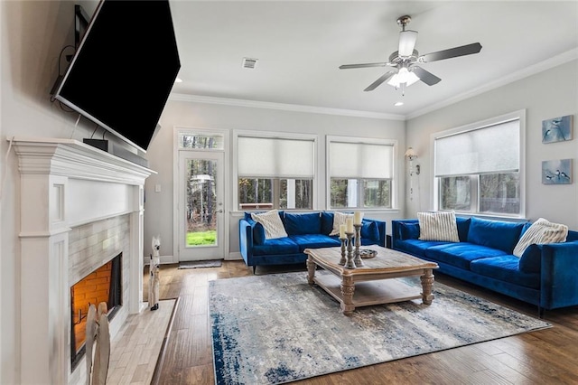 living area featuring visible vents, a tiled fireplace, ornamental molding, wood finished floors, and baseboards