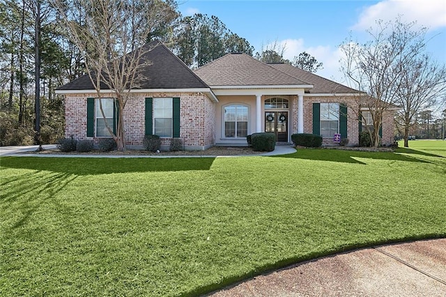 view of front facade featuring a shingled roof, a front lawn, and brick siding