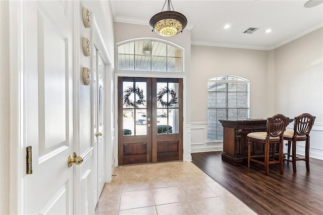 entryway with light wood-style flooring, a decorative wall, a wainscoted wall, visible vents, and ornamental molding