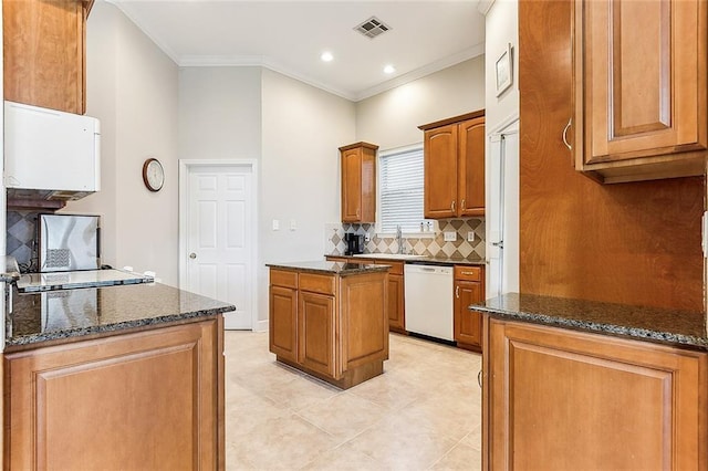 kitchen with visible vents, dark stone counters, dishwasher, a kitchen island, and ornamental molding