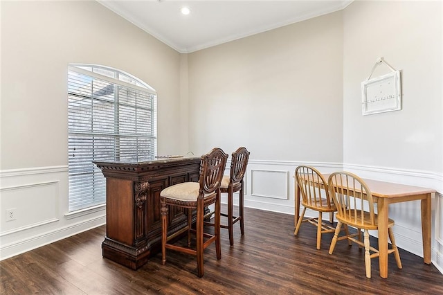 dining space featuring a wainscoted wall, a decorative wall, ornamental molding, dark wood-type flooring, and a bar