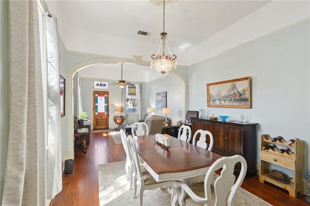 dining area featuring arched walkways, ceiling fan with notable chandelier, dark wood-style floors, and visible vents