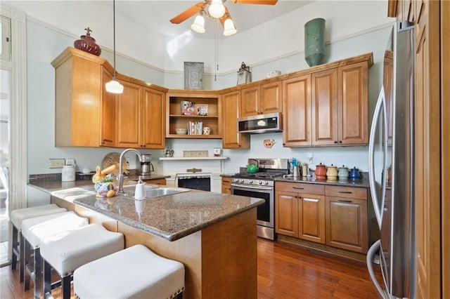 kitchen with a peninsula, stainless steel appliances, brown cabinetry, a kitchen bar, and decorative light fixtures