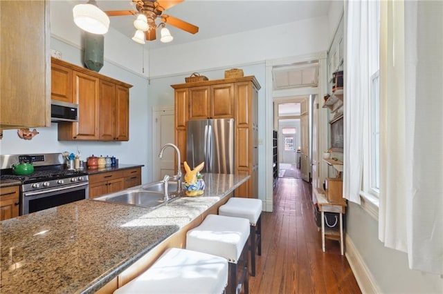 kitchen featuring appliances with stainless steel finishes, brown cabinetry, a sink, and a kitchen breakfast bar